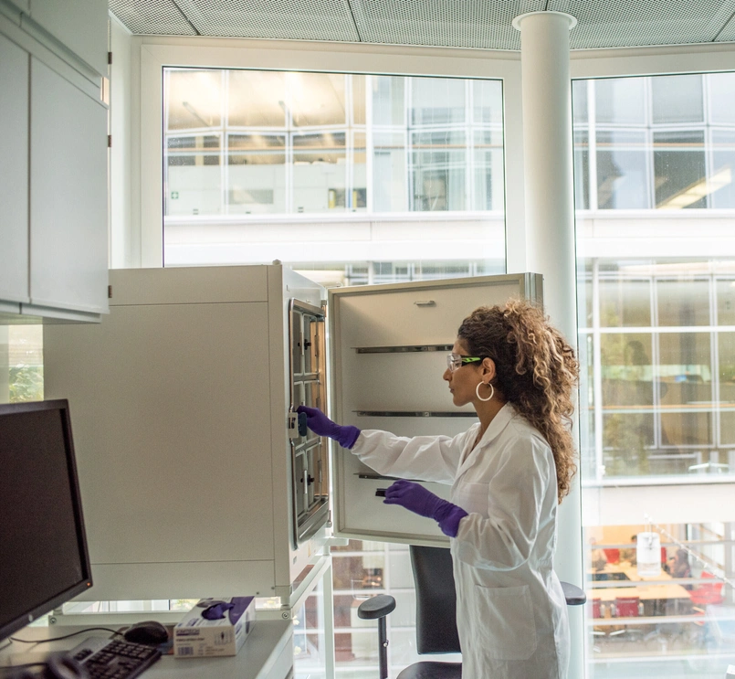 A scientist in a lab coat searching for items in an open cupboard