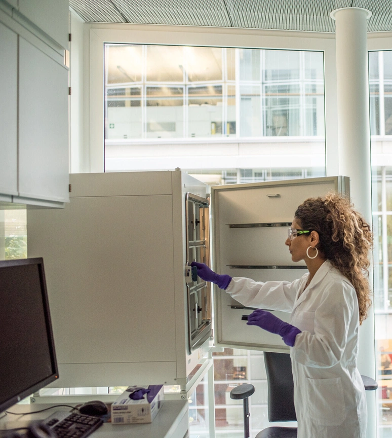 A scientist in a lab coat searching for items in an open cupboard