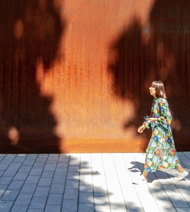 A woman walking past the high walls of the Dirk's Pod structure on campus