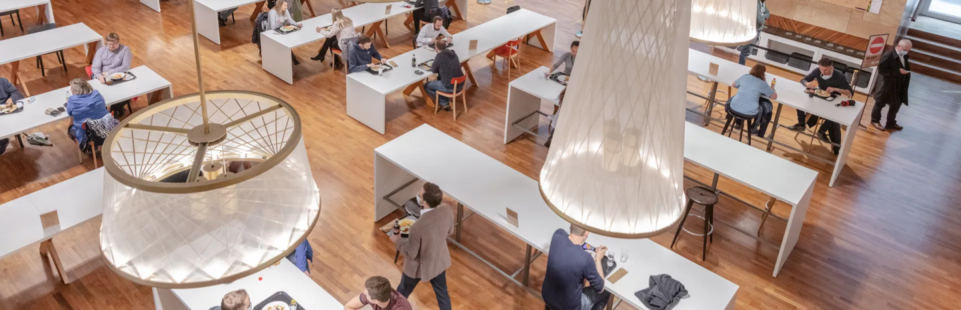 People eating and talking to each other in an spacious, well-lit communal canteen