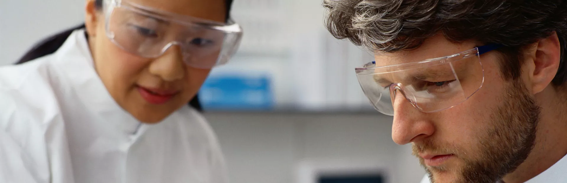 Two scientists wearing lab coats and goggles working together