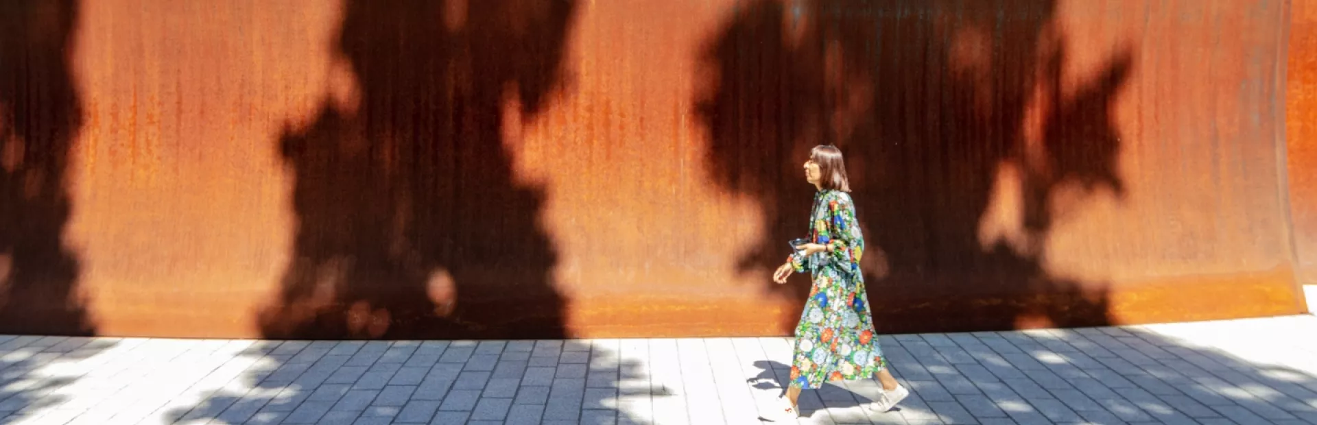 A woman walking past the high walls of the Dirk's Pod structure on campus