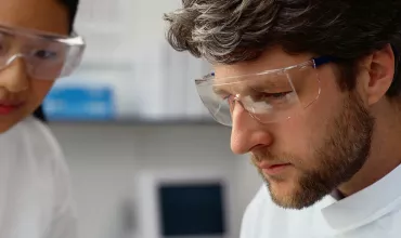 Two scientists wearing lab coats and goggles working together