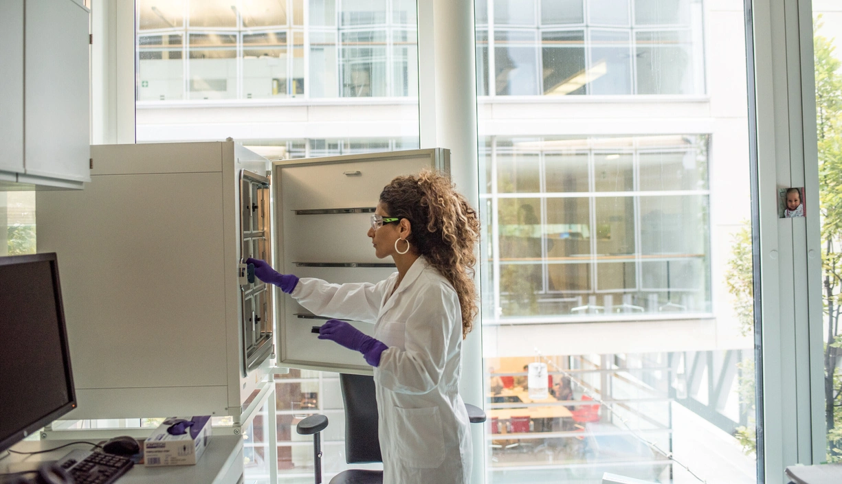 A scientist in a lab coat searching for items in an open cupboard